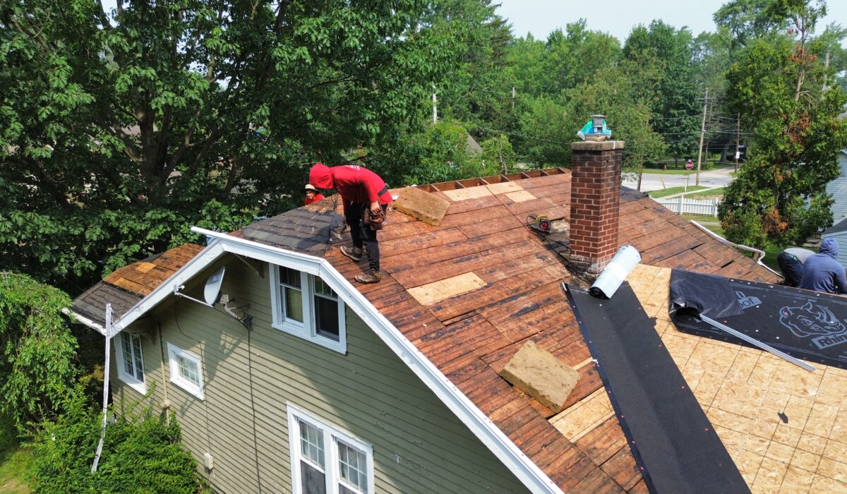 Roofing crew tearing off shingles to inspect wood decking after storm damage.