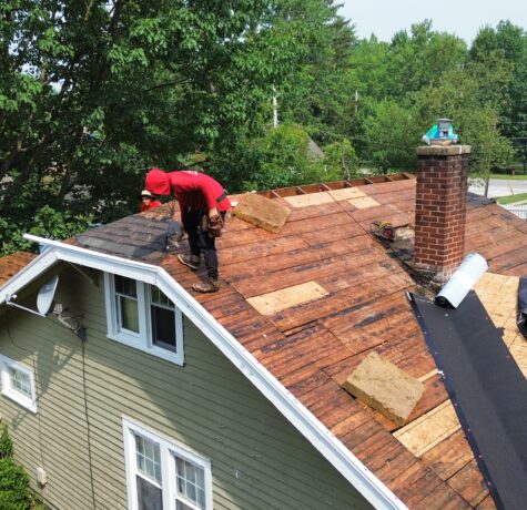 Roofing crew tearing off shingles to inspect wood decking after storm damage.