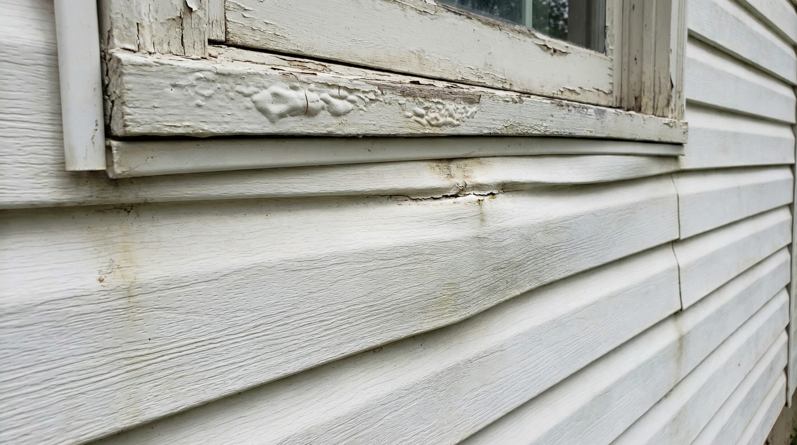 Close-up of bulging vinyl siding with paint bubbling around window frame